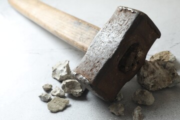 One sledgehammer and pieces of broken stones on grey textured background, closeup