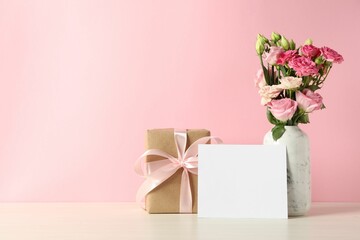 Happy Mother's Day. Gift box, blank card and bouquet of beautiful flowers in vase on white table against pink background. Space for text