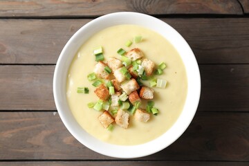 Tasty potato soup with croutons and green onion in bowl on wooden table, top view