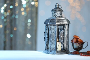 Arabic lantern, misbaha and dates on table against blurred lights, space for text