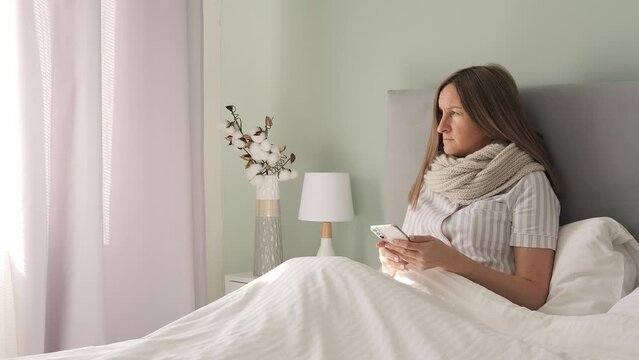Stricken by illness in bed woman battles disease her phone lifeline. Disease weighs heavy yet she seeks comfort in digital world. With each swipe diseases grip loosens offering brief respite in pixels