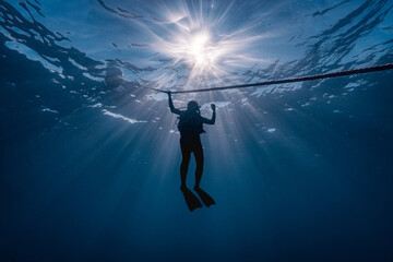 silhouette of a diver down deep with sunlight at background