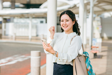駅・ステーションのロータリーでスマホを使う女性（アプリ・モバイルチケット・チケットレス・電子乗車券）  © buritora