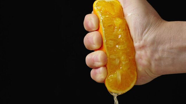Woman's hand squeezing half a juicy orange on black background in slow motion.