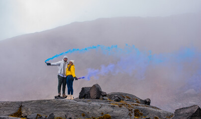 pareja de mujeres sonriendo y usando abrigos coloridos en una piedra del volcan y humo de color azul