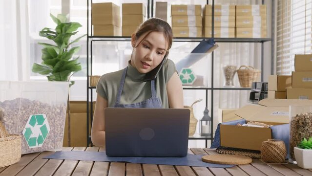 Asian SME owner go green net zero waste retail store shop busy talk mobile phone call eco packaging box design. Asia people young adult woman happy work at home office desk smart vendor seller order.