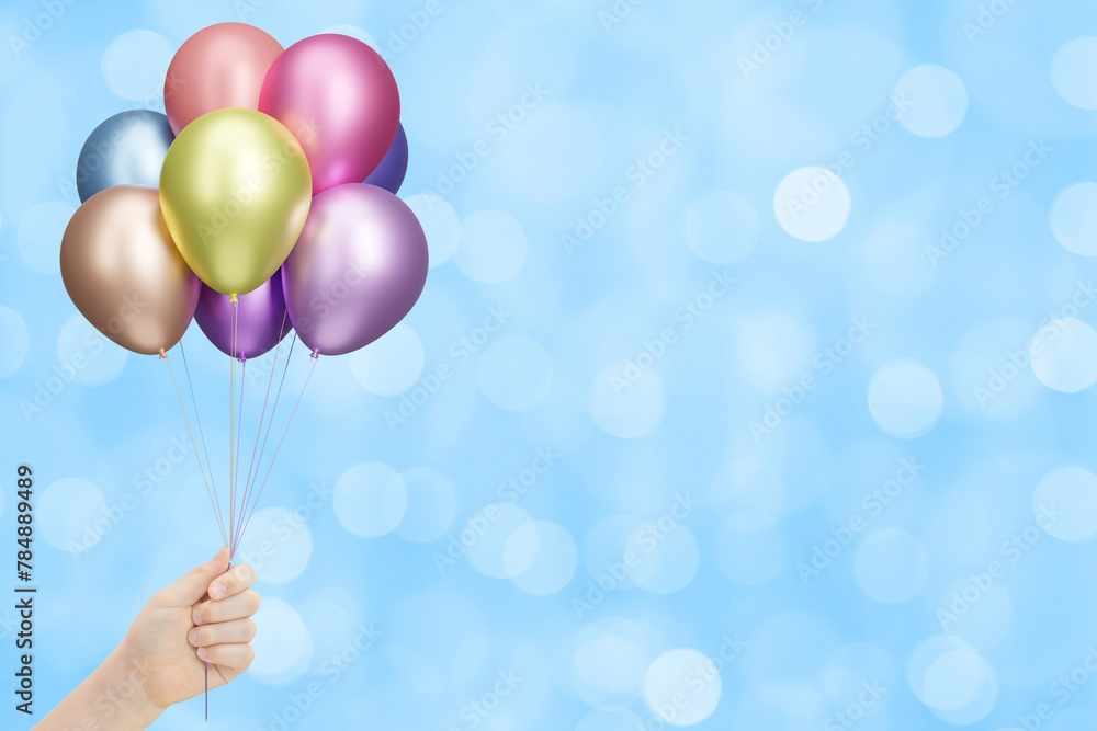 Aufkleber Female hand holds bunch of colorful shiny balloons on blurred blue background. Empty space for text