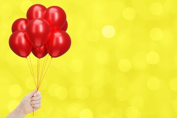 Female hand holding bunch of shiny red balloons on blurred yellow background. Empty space for text - 784889490