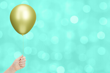 Сhild's hand holding the yellow or golden balloon on blurred green background. Empty space for text