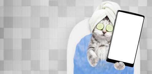 Kitten with towel on it head, with pieces of cucumber on it eyes and with cream on it face takes...