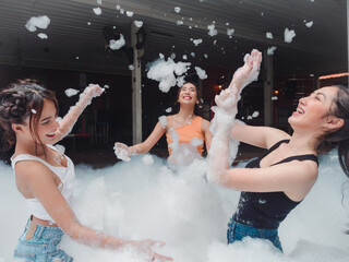 Portrait of three pretty young woman in bikini having fun on soap foam disco party in the swimming pool..