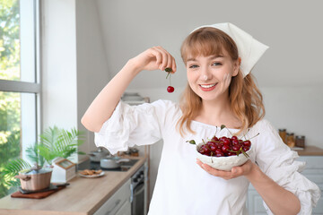 Beautiful happy young woman with bowl of cherries in kitchen