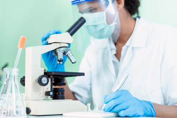 Indian Scientist man look into Microscope research in science laboratory. Asian biochemistry scientist using microscope in laboratory chemistry labs. Covid-19 medical research scientific experiment