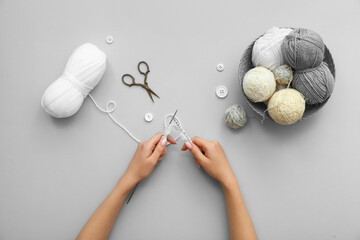 Woman knitting with yarn balls and scissors on grey background
