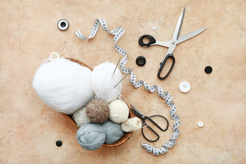 Basket with yarn balls, scissors and knitting accessories on beige grunge background