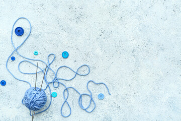 Yarn ball with knitting needles and buttons on blue grunge background