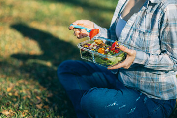 On a beautiful day, a woman enjoys a picnic in the park, The spread includes a glass lunch box...