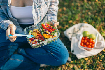 On a beautiful day, a woman enjoys a picnic in the park, The spread includes a glass lunch box...