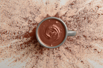 Cup of tasty melted chocolate with cocoa powder on grey background