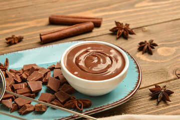 Bowl of tasty melted chocolate, star anise and cinnamon sticks on wooden background