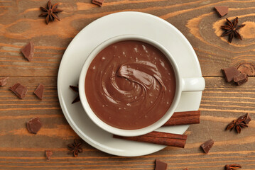 Cup of tasty melted chocolate with cinnamon sticks and star anise on wooden background