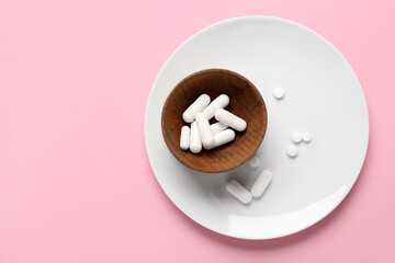 Plate and wooden bowl with different pills on pink background