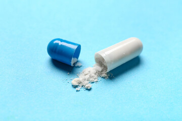 Opened capsule with powder on blue background