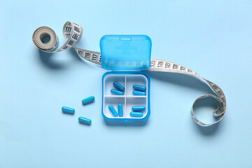 Container with weight loss pills and measuring tape on blue background