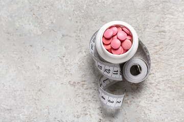 Bottle with weight loss pills and measuring tape on grey grunge background