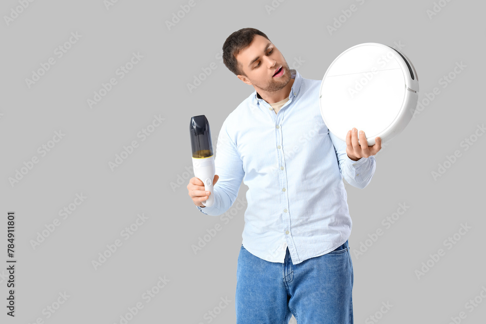 Poster Handsome man with handy and robot vacuum cleaners on light background