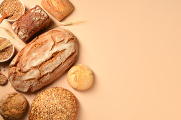 Loaves of fresh bread with buns and wheat spikelets on beige background