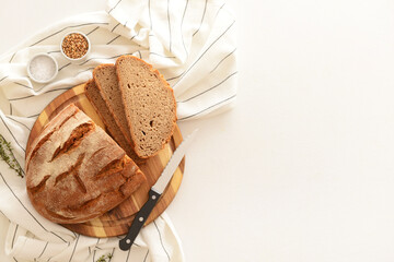 Wooden board with sliced loaf of bread, wheat grains, thyme and knife on white background