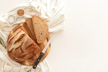 Foto auf Acrylglas Wooden board with sliced loaf of bread, wheat grains, thyme and knife on white background © Pixel-Shot
