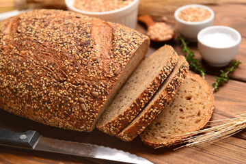 Sliced loaf of bread, wheat spikelet and knife on wooden background