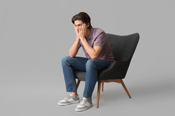 Weary young man sitting in armchair on light background