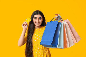 Happy smiling young woman with shopping bags and credit card on yellow background