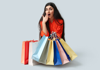 Surprised young woman with shopping bags sitting on white background