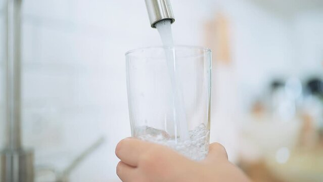 Hand of Asian woman pouring clean tap drinking water into the clean glass in kitchen room