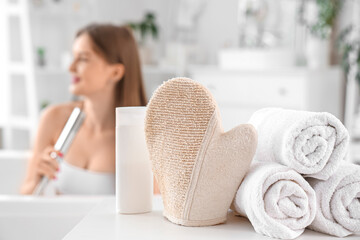 Massage glove with towels and shower gel on table in bathroom, closeup