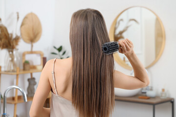 Fototapeta premium Young woman brushing her hair in bathroom, back view