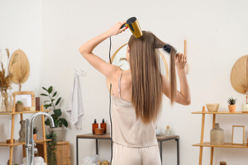 Young woman drying her hair with round brush in bathroom, back view