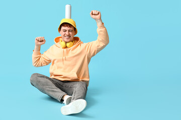 Happy young man with can of soda on his head against blue background