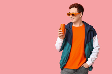 Young man in sunglasses with can of soda on pink background