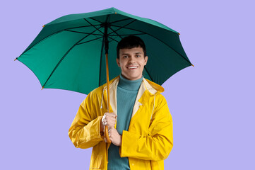 Young man in raincoat with green umbrella on lilac background