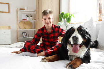 Little boy with Bernese mountain dog sitting in bedroom