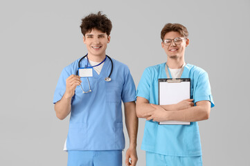 Male medical interns with badge and clipboard on light background