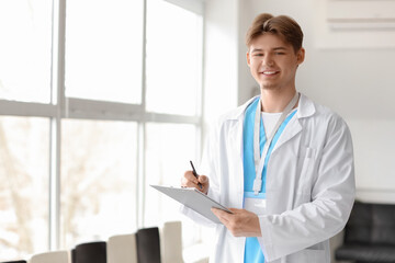 Male medical intern with clipboard near window in clinic