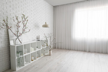 Vases with blooming branches on shelving unit near white brick wall