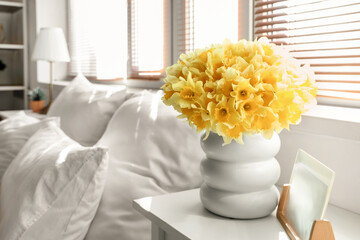 Vase with daffodils and frame on table in bedroom