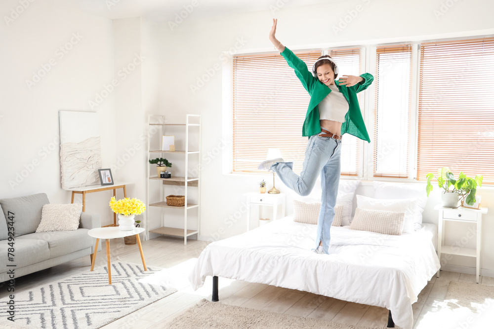 Wall mural young woman in headphones dancing on bed at home